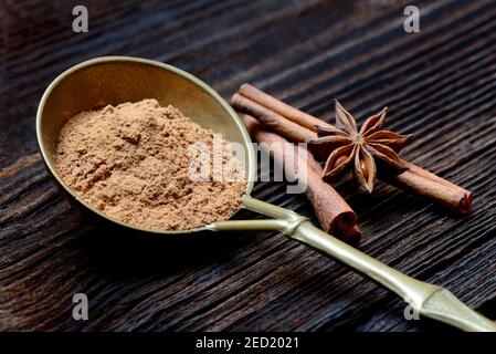 Cinnamonpowder ( Cinnamomum spec.) in brass ladle and star anise sticks Stock Photo