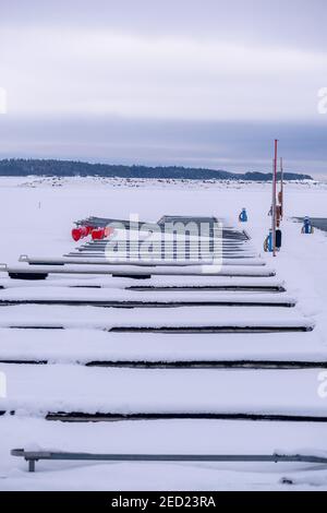 Helsinki / Finland - FEBRUARY 14, 2021: A view of an empty leisure boat harbor in the middle of winter. A frozen lake with an island in the background Stock Photo