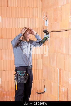 An electrician at work thinking what start to install first in sockets in unfinished house built of clay block bricks. Worker ready for wiring cables Stock Photo