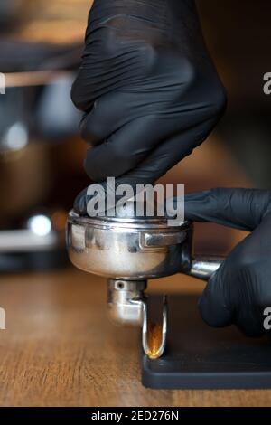 barista hands temping coffee grind in espresso holder during coffee preparation, closeup Stock Photo