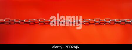 Long silver colored chain on red background with reflection. Abstract panoramic image Stock Photo