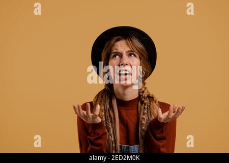 Photo of cute female farmer looks disappointed. White woman wears denim overall and hat isolated brown color background Stock Photo