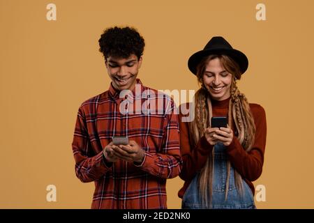 Photo of black male and white female farmers watch their smartphones. Man wears plaid shirt, Woman wears denim overall and hat isolated brown color Stock Photo