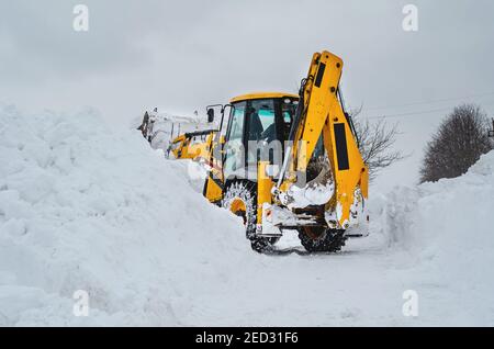 Yellow tractor excavator with a large bucket clears a snowy road from snow Stock Photo
