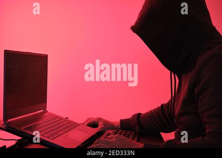 Hooded hacker in front of a computer for organizing massive data breach attack around the world. Cyber criminal concept. Stock Photo