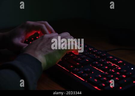 Hands typing on a red lighting keyboard on dark background. Cyber criminal concept. Stock Photo