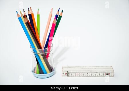 Many colored crayons form a bouquet of flowers on a white background, near it is placed one meter to indicate compliance with the safe distance. Stock Photo