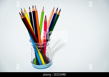 Many colored crayons are inside a transparent container and form a bouquet of flowers on a white background, plenty of space available for text. Stock Photo