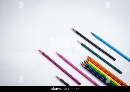 Many colored crayons are placed in an inclined position like arrows on a white background, ample space available for text. Stock Photo