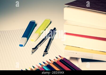 Two highlighters and a compass are placed on a square sheet, in the foreground a stack of books and colored crayons. Stock Photo