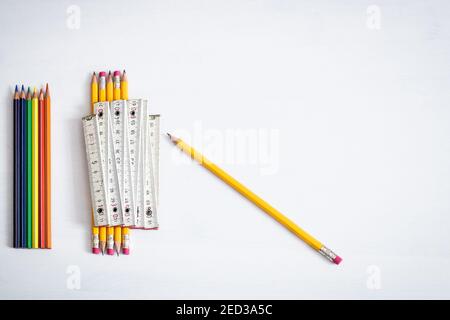 A group of coloured crayons and pencils resting on a white background with one meter indicating the safe distance to keep in enclosed places. Stock Photo