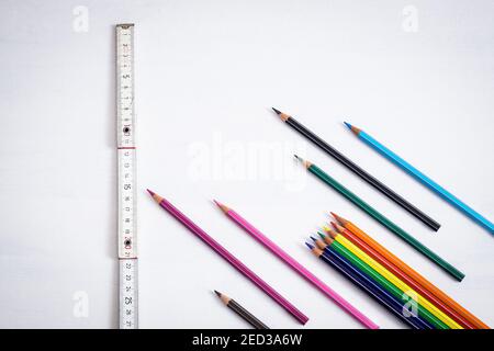 Many colored crayons placed like arrows on a white background, a nearby wooden meter indicates the safe distance to keep in the classrooms to prevent Stock Photo