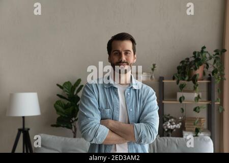 Happy young male standing in living room with arms crossed Stock Photo