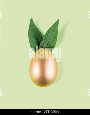 Easter egg painted in gold color with green bunny ears. Happy Easter minimalistic background. Stock Photo
