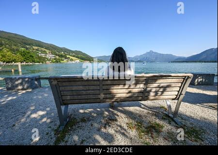 A woman is sitting on a bench and looking over lake Mondsee in Austria Stock Photo