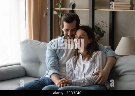 Young husband sit on couch hold beloved wife in arms Stock Photo