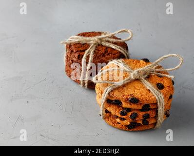 Stacks of homemade raisin oatmeal cookies and dark chocolate chip cookies tied in string on a gray concrete surface. Copy space. Close-up. Stock Photo