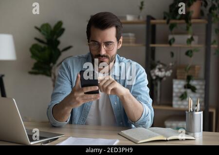 Serious young guy student check uncertain information online using smartphone Stock Photo