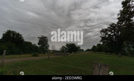 dark structured clouds over hiking path on pasture in the morning, Germany Stock Photo