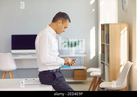 Serious businessman standing in the office and using finance app on his mobile phone Stock Photo