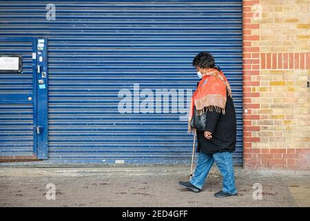 A black lady wearing a face mak walks with a walking stick Stock Photo