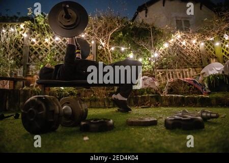 During lockdown in 2021, with gyms closed, a teenage boy trains in the garden in an improvided gym on a winter evening Stock Photo