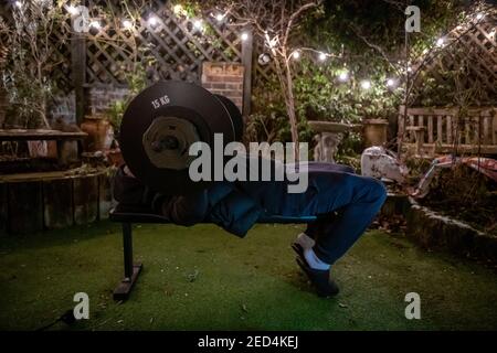 During lockdown in 2021, with gyms closed, a teenage boy trains in the garden in an improvided gym on a winter evening Stock Photo