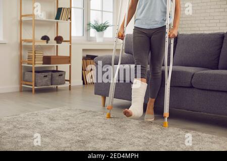 Woman with broken injured leg in cast standing with metal crutches during rehabilitation at home Stock Photo