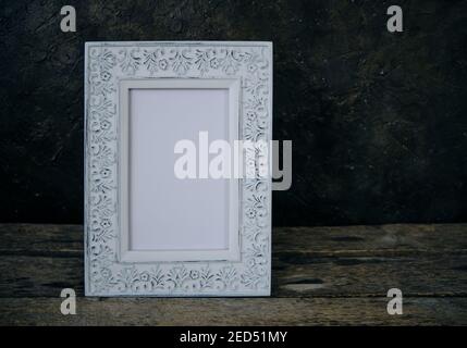 An old, worn, retro photo frame on a wooden table against a concrete wall Stock Photo