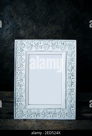 An old, worn, retro photo frame on a wooden table against a concrete wall Stock Photo