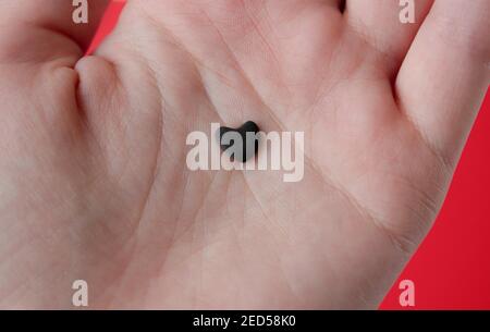 Small gray stone in the shape of a heart in a female hand on a red background. Stock Photo