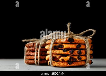 Stacks of homemade oatmeal and chocolate biscuits tied with a rope lie on a gray concrete surface against a black background. Close-up, copy space. Stock Photo