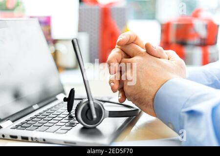 Men's folded hands in front of a laptop with a headset close-up. The concept of remote work. Stock Photo