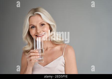 Smiling healthy thirsty fit mid aged 50s woman holding glass drinking water. Stock Photo