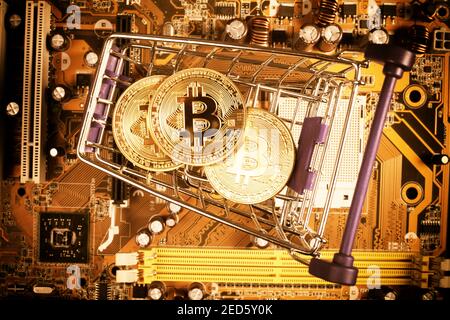 golden bitcoins in a cart from a supermarket on a computer board, close-up, tinted orange. Stock Photo