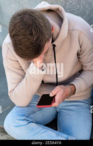 Guy sitting and holding phone. Portrait of man with smartphone in his hands. Vertical frame. Stock Photo