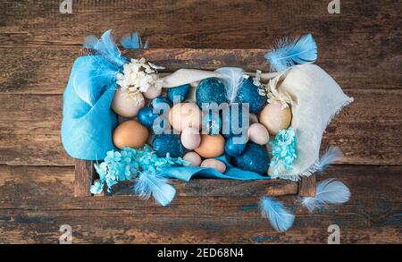 A box with Easter eggs in blue and natural colors on a wooden background. Stock Photo