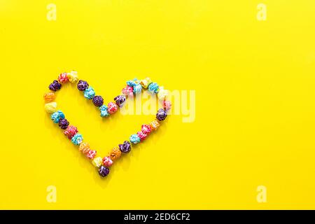 Colored popcorn. Heart shape made of colored popcorn, flat lay on yellow background with copy space, Stock Photo