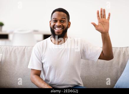 Cheerful African American Man Waving Hand Sitting On Couch Indoor