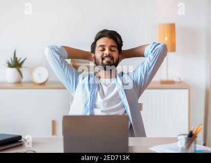 Smiling Arab Freelancer Guy Leaning In Chair, Relaxing After Working On Laptop Stock Photo
