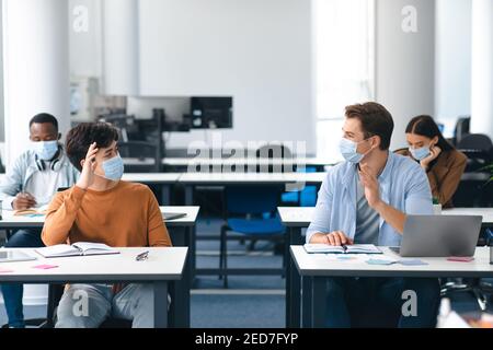 Diverse students wearing face masks greeting and waving Stock Photo
