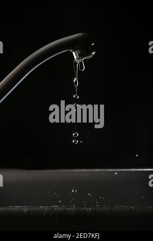 Leaking tap water against a black background, due to the tap being open Stock Photo