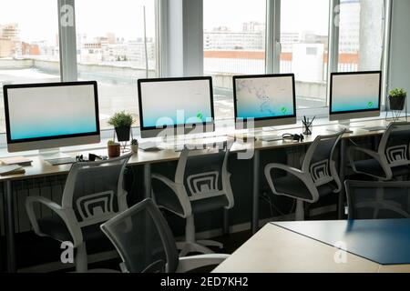 Row of computer monitors standing on desks against large windows inside contemporary empty call center at the end of working day Stock Photo