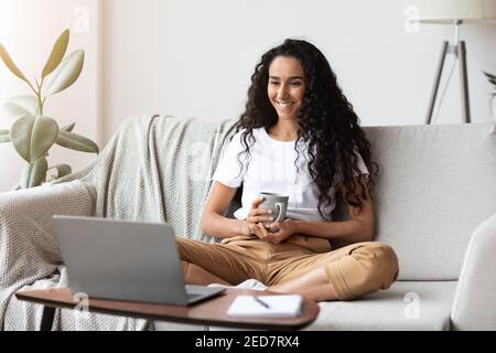 Happy woman with cup of coffee watching movie online Stock Photo