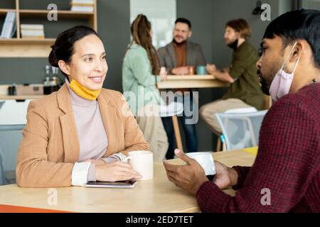 Two small groups of young intercultural designers or managers having coffee and discussing working plans or creative ideas at break Stock Photo