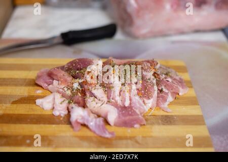 raw meat pork on a cutting wooden board, sprinkled with seasonings, next to a knife, selective focus Stock Photo