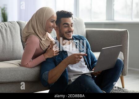 Excited arab guy showing something his girlfriend on Internet Stock Photo