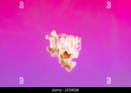 Close up of piece popcorn on pink purple background. Concept of popcorn. Stock Photo