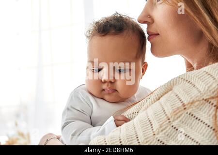 Loving caucasian mother hugging cute infant african american baby daughter. Stock Photo