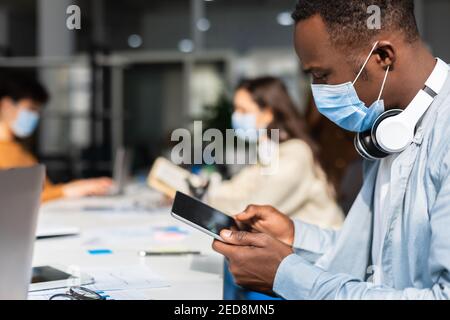 Black man in mask sitting at desk using tablet Stock Photo